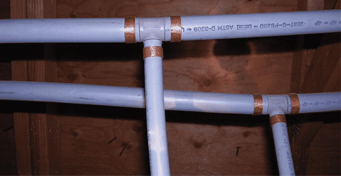 Grey Poly-B water pipes under a floor, joined with grey plastic fittings and copper crimp rings, with PB2110 printed on the pipe